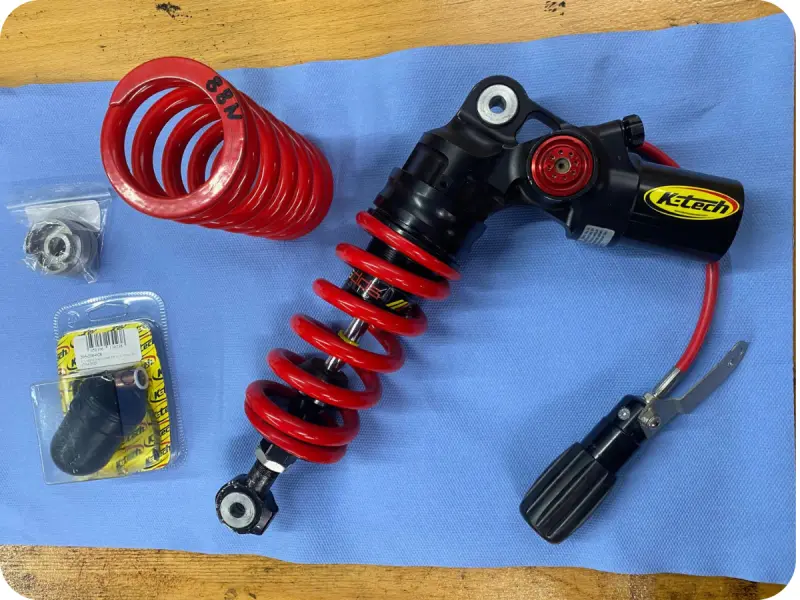 K-Tech Motorrad-Federbein mit roter Feder und externem Reservoir, zur Wartung auf blauer Werkbank – Fahrwerksservice bei BikeTech Lohmann in Walsrode.