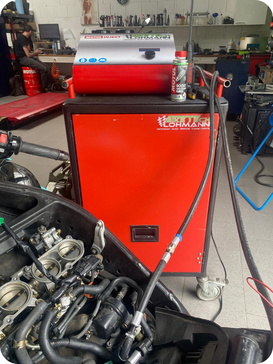 MOTUL INJECT Gerät auf rotem BikeTech-Lohmann-Servicewagen mit angeschlossenen Schläuchen; Einspritzanlage/Throttle-Bodies eines Motorrads im Vordergrund in der Werkstatt.